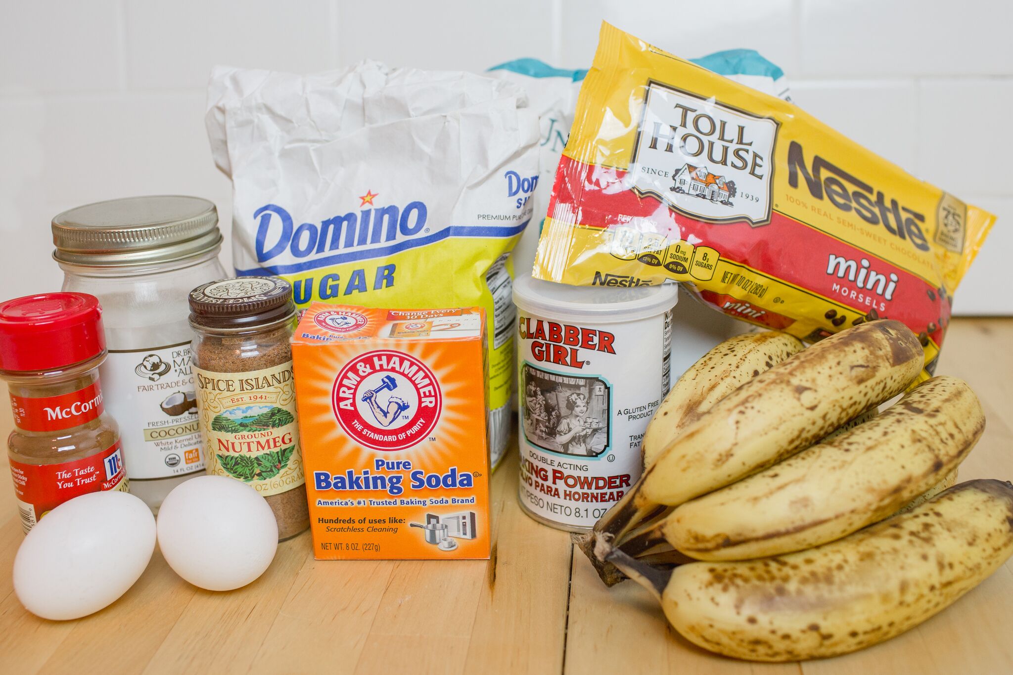 Assemble your ingredients for the chocolate chip banana bread: Cinnamon, eggs, coconut oil, nutmeg, baking soda, baking powder, sugar, flour, ripe bananas and mini chocolate morsels.