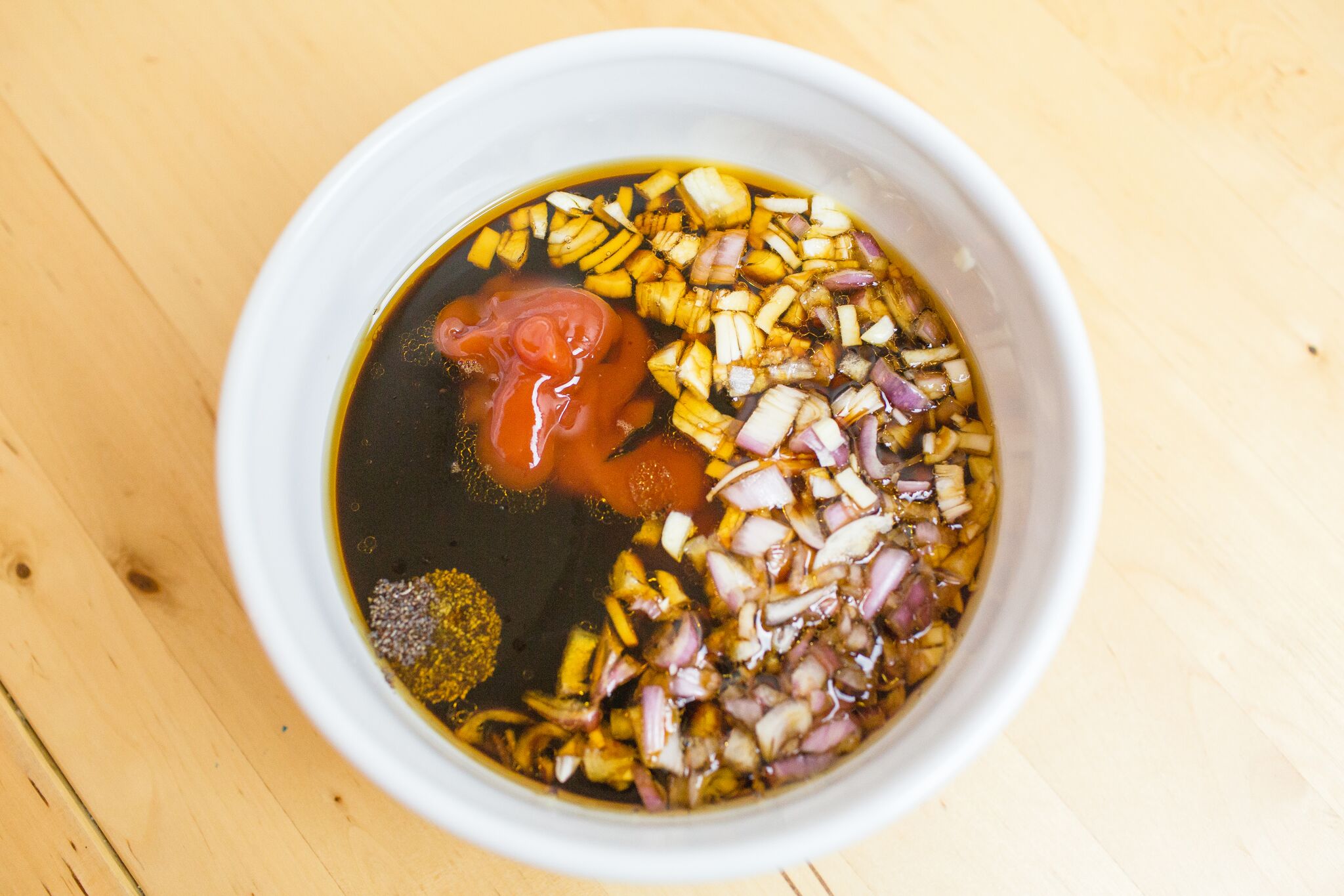 Whisk sesame oil, soy sauce, chopped garlic, shallot, liquid smoke, black pepper, ketchup, and maple syrup together in bowl.